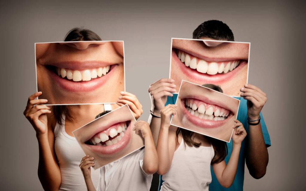 young family with children holding a picture of a mouth smiling on a gray background